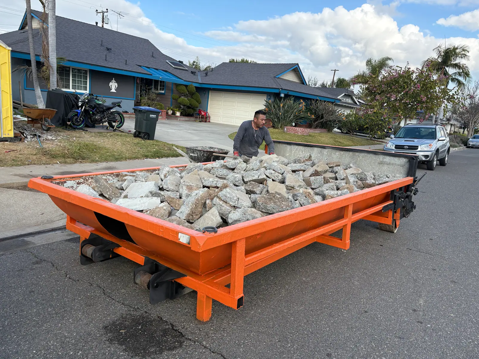Orange dump trailer loaded with broken concrete, crew member behind it