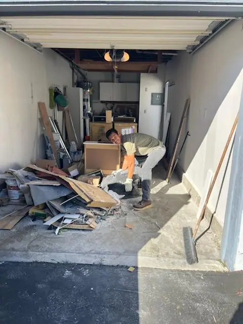 Garage floor covered in boards, boxes and debris with a crew member starting to clear it