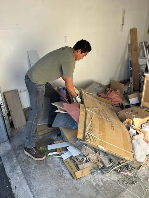 Crew member clearing a pile of cardboard and scrap from a garage
