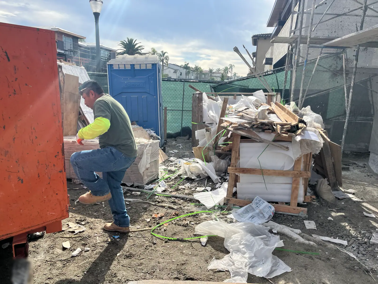 Crew member stepping into a debris bin next to a pile of packaging and pallets