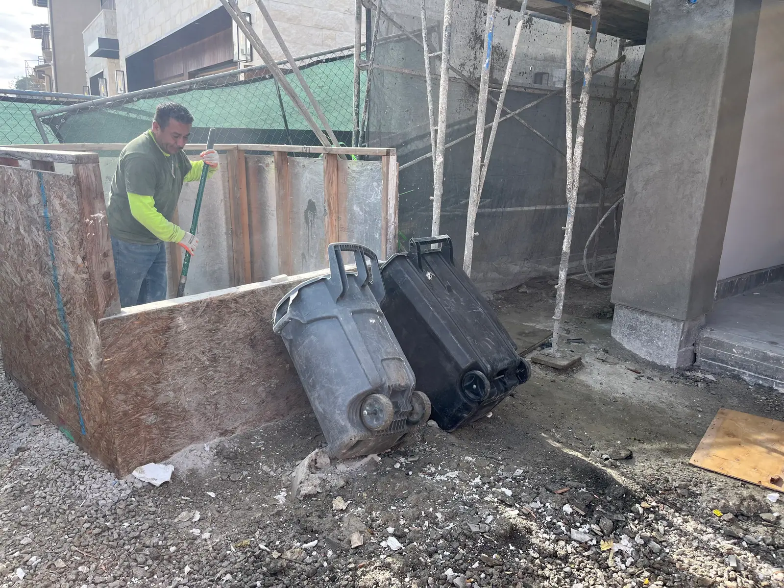 Smiling crew member raking debris inside a plywood bin at a jobsite